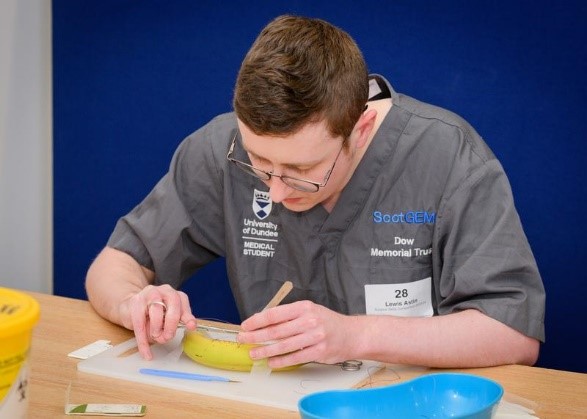 Medical student wearing scrubs suturing a banana